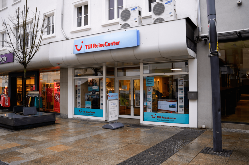 Straßenansicht eines TUI ReiseCenters bei Tageslicht mit Eingang und Glasfront.